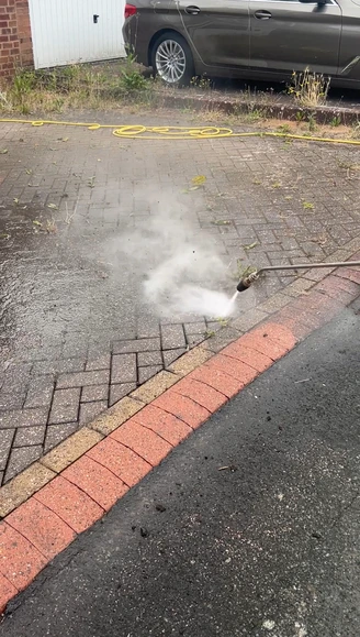 Professional pressure washing wand blasting away weeds and grime on block paving in Dudley.